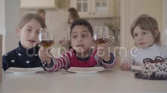 三个孩子在桌子上拿着小蛋糕和果汁眼镜两个女人在后台说话二视频的预览图