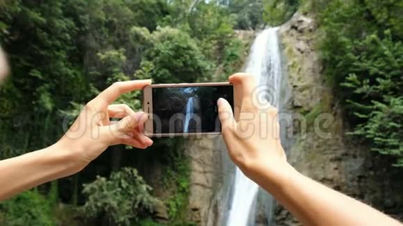 女人专注于手机屏幕拍摄瀑布特写照片视频的预览图