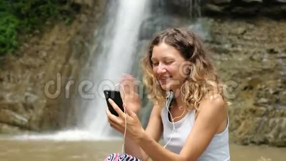女人挥动手机通过视频链接用耳机交谈并显示瀑布视频的预览图