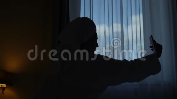穿浴袍的女孩坐在床上的酒店窗户前视频的预览图