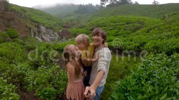 慢镜头年轻夫妇和他们的儿子站在山上的一个大茶园里自拍视频的预览图