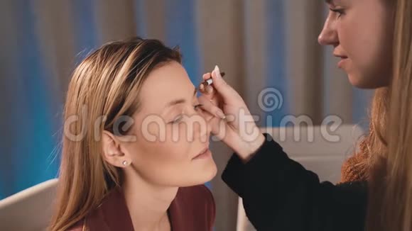 化妆师用铅笔在白种人金发模特的脸上画并诱导眉毛的形状化妆视频的预览图