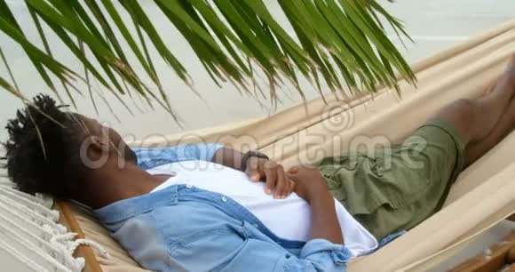 从4k海滩的吊床上睡觉的非裔美国人的高角度视角视频的预览图