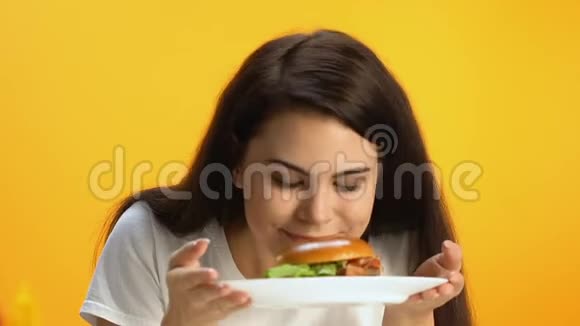 美丽的黑发女人嗅着美味的汉堡微笑着快餐油腻的饭菜视频的预览图