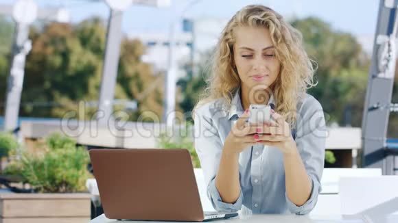 年轻漂亮的女商人在咖啡馆工作它使用手机和笔记本电脑视频的预览图