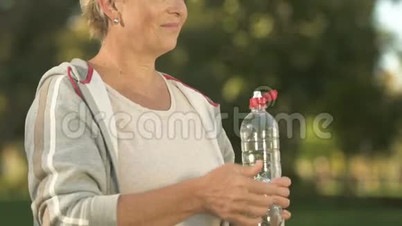 快乐的老年妇女喝着水相机微笑训练后放松视频的预览图
