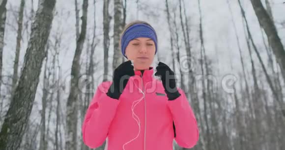 晨冬慢跑前的女人在耳朵里插入耳机准备穿过自然公园视频的预览图