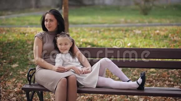 年轻的母女正在一个城市公园里的长凳上休息一个幸福的家庭视频的预览图