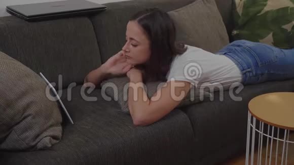 年轻女子躺在沙发上看平板电脑上的电影视频的预览图