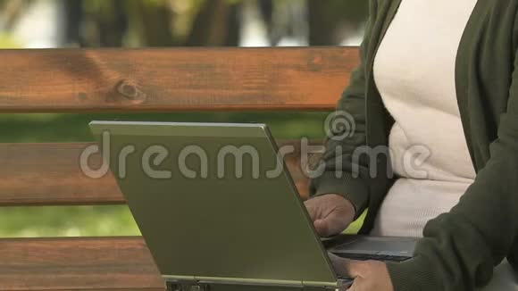 女性养老金领取者在笔记本电脑上打字坐在公园公共无线上网视频的预览图