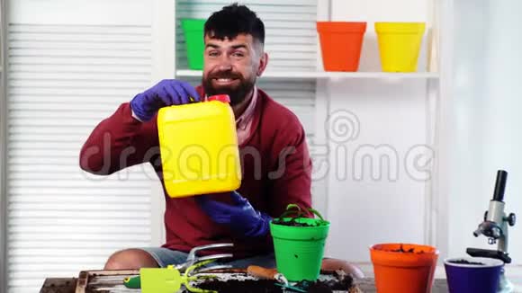 满脸胡须的男人手里拿着一个塑料罐另一只手里拿着一个带植物的罐子园艺视频的预览图