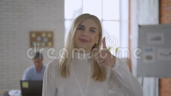 一个蓝眼睛金发女孩的肖像友好的办公室工作人员伸出大拇指团队合作概念4K视频的预览图