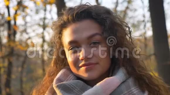 白种人卷曲头发的女人在秋天公园背景下观看并转向相机的肖像视频的预览图