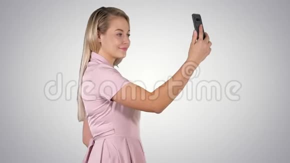 年轻漂亮的女人在梯度背景下在手机上自拍视频的预览图