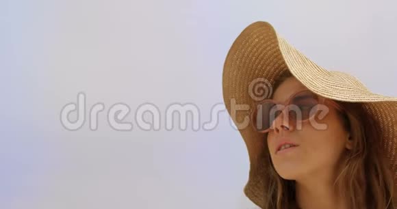 戴着帽子和太阳镜的白人妇女站在海滩上的正面景色视频的预览图