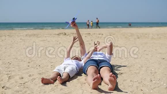 妇女和一个孩子躺在沙滩上背景是大海妈妈和小男孩玩玩具飞机视频的预览图