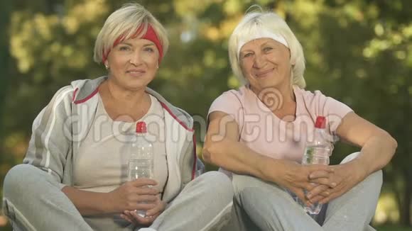 微笑着穿着运动服的退休妇女拿着水瓶看着镜头视频的预览图