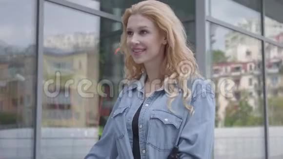 年轻的苗条迷人的金发女人穿着白色牛仔裤带着她的自行车靠近城市的商店窗户性感的女人视频的预览图