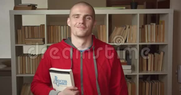 年轻有魅力的白种人男学生的特写肖像他拿着一本书看着相机在大学里微笑视频的预览图
