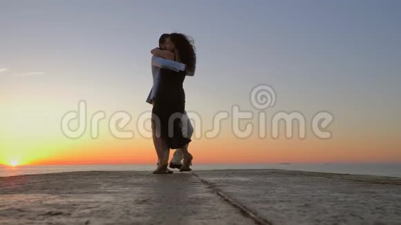 精力充沛的西班牙夫妇在日出和海洋的背景下展示了性感拉丁舞的元素视频的预览图