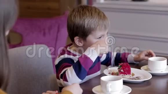 侧景有趣的小男孩和美丽的年轻母亲喝茶吃蛋糕视频的预览图