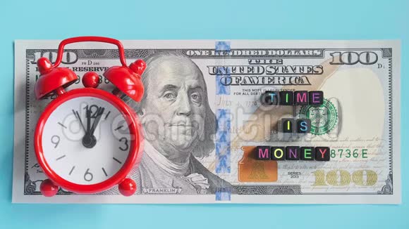 多色文字时间是金钱和红色闹钟走滴答的背景上的美国数百美元钞票特写康塞普视频的预览图