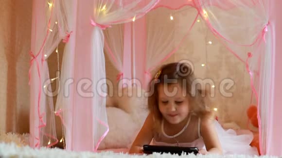 小女孩在卧室里用平板电脑孩子在电脑屏幕上看视频在她的房间里玩视频的预览图