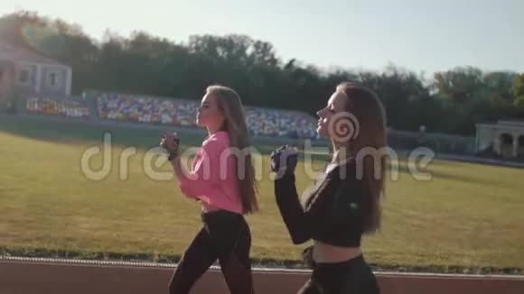 两名健身跑步女运动员在运动场跑道上慢跑在炎热的夏季早晨开放空气视频的预览图