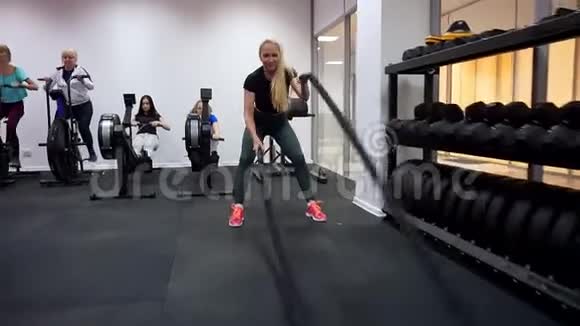 在交叉健身高强度间歇训练中一名妇女积极参与使用战斗绳索的健身房锻炼视频的预览图
