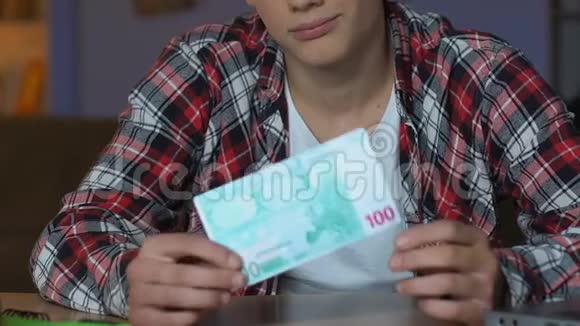 拿着欧元钞票坐在家里的桌子上的男学生经济责任视频的预览图