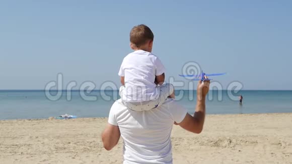 父亲把孩子抱在肩上快乐父子推出玩具飞机一家人在海边休息视频的预览图