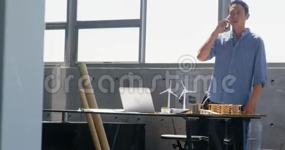 亚洲男性建筑师在现代办公室用手机交谈的正面景色视频的预览图