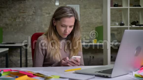 在工作场所使用笔记本电脑旁的电话特写漂亮的高加索女员工视频的预览图