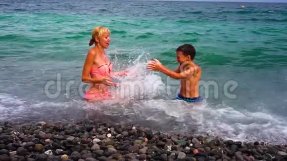年轻苗条的母亲和她的儿子在海滩上玩得很开心动作很慢夏天在卵石海岸的家人视频的预览图