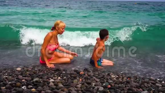 年轻苗条的母亲和她的儿子在海滩上玩得很开心动作很慢夏天在卵石海岸的家人视频的预览图