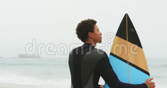 非洲裔美国男性冲浪者在海滩上站着冲浪板的后视图视频的预览图