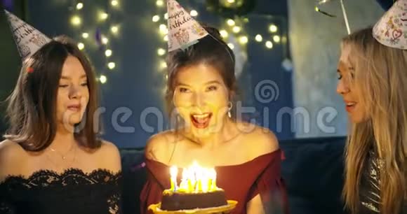 漂亮的微笑女孩在一个聚会上在朋友围着的生日蛋糕上吹蜡烛围绕着视频的预览图