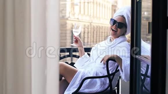 女人头上戴着毛巾穿着浴袍坐在阳台上端着一杯香槟视频的预览图