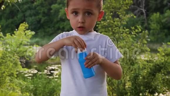 一个孩子在湖底的绿色公园里吹肥皂泡视频的预览图