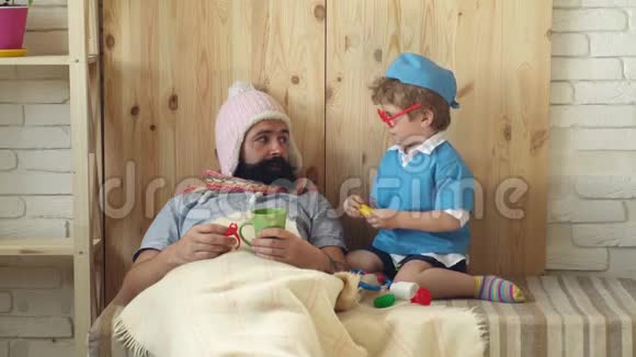小医生用药片治疗躺在毯子下面的病人男孩和他父亲扮演医生概念视频的预览图