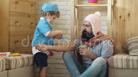 穿着医生衣服的男孩使一个胡子病人父子俩在医院玩健康观念视频的预览图