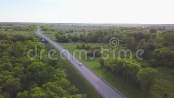 在夏季俄罗斯乡村道路和移动汽车的空中景观被绿树和蓝色的田野包围着视频的预览图