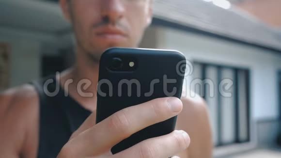 关闭男子使用智能手机户外有平板电脑的年轻人一个男人在社交网络附近的院子里视频的预览图