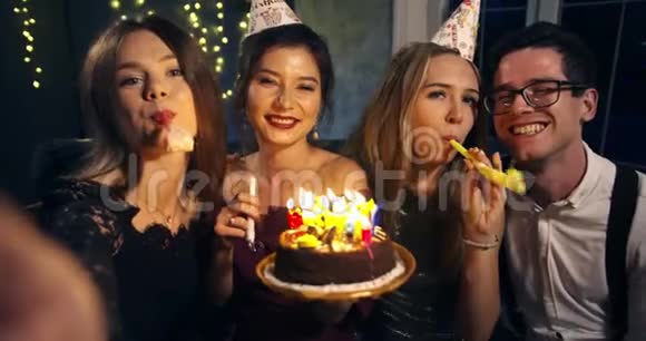 漂亮的微笑女孩在一个聚会上在朋友围着的生日蛋糕上吹蜡烛围绕着视频的预览图