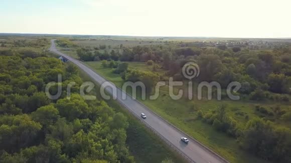 在夏季俄罗斯乡村道路和移动汽车的空中景观被绿树和蓝色的田野包围着视频的预览图