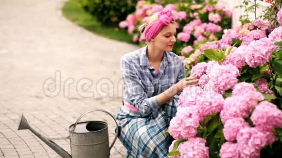 头上戴着粉红色丝带的女孩关心花有浇水罐的女人在花园里种花视频的预览图
