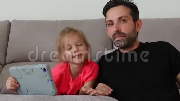 父亲和女儿和平板电脑有关坐在沙发上视频的预览图