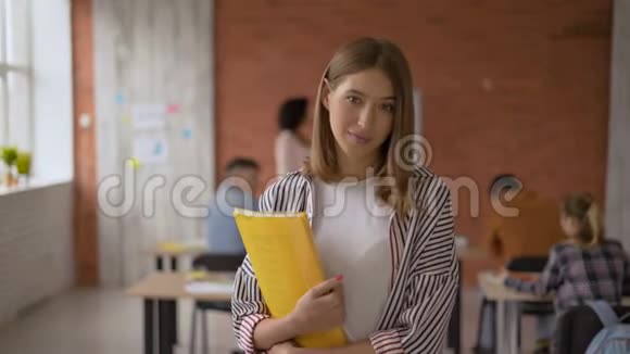 调情的女学生手里拿着一个黄色的文件夹女人对着相机微笑教室里的学生4K视频的预览图