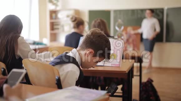 一个坏学生在课桌下上课时玩智能手机躲着老师教师观察如何视频的预览图