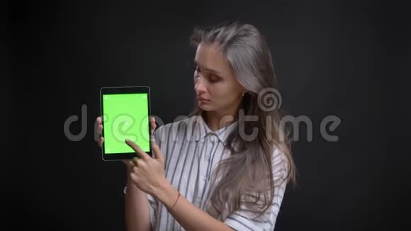 美丽的白种人长发妇女的肖像显示绿色屏幕的平板电脑相机在黑色背景视频的预览图